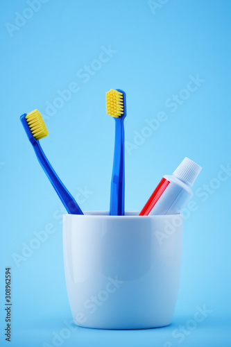 Toothbrushes and a toothpaste tube in a holder cup against blue background