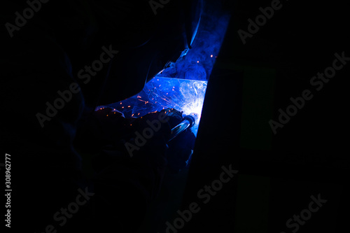 Masked welder works at the factory on metal welding. Sparks and smoke fly. Industrial photo.