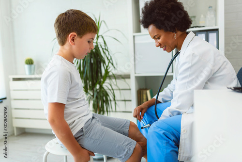 Woman African American doctor general practitioner examining child s patellar knee-jerk reflex