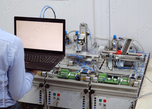 Engineer is programming PLC with his laptop for a smart factory prototype. Industry 4.0 workshop in an automation education center. Engineer is learning how to program a PLC. Selective focus.