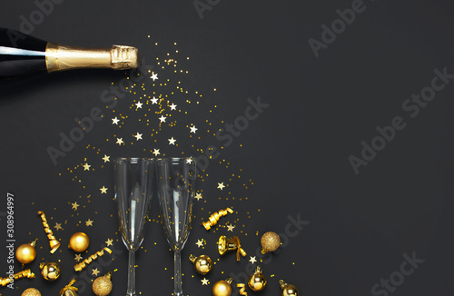 Christmas and New Year background. Champagne bottle champagne glasses golden christmas balls festive ribbons star confetti on black background top view. Flat lay holiday card. Party decorations 2020
