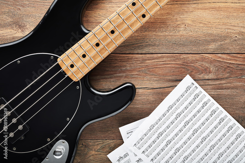 Black bass guitar with headphones and sheet music on wooden table