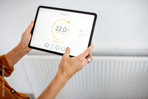 Controlling radiator heating temperature with a tablet, close-up with radiator on the background. Concept of a smart home and mobile application for managing smart devices at home