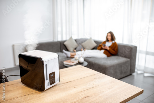Photos Woman relaxing on the couch at home with working air humidifier on the foreground