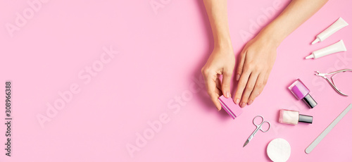 Stylish beautiful gentle manicure. Hands of young woman with nail file, manicure tools on pink background top view flat lay. Natural nails gel polish self-care beauty and fashion. Nail care salon spa