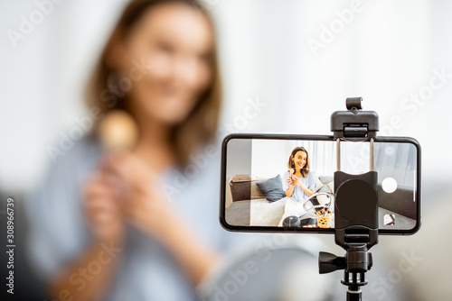 Young woman recording on a smart phone her vlog about cosmetics, showing and demonstrating makeup, close-up on phone. Influencer marketing in social media concept photo