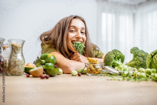 Portrait of a young cheerful woman with pea seedlings and lots of healthy green food on the table. Concept of vegetarianism and well-being