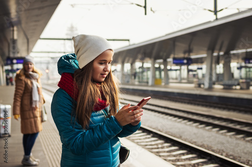 Canvas Print Woman is standing at railroad station and buying a railway ticket on her smart phone