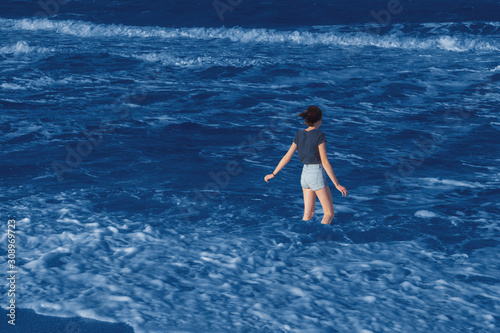 Color of the year 2020 classic blue. Tween girl standing on beach against stormy waves. Young woman spending weekend at sea. Trip to seaside, summer vacation. Fashionable pantone color trend concept