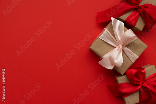 Gift boxes wrapped brown craft paper and red and pink ribbon on red background. Valentines day or Christmas celebration concept. Top view