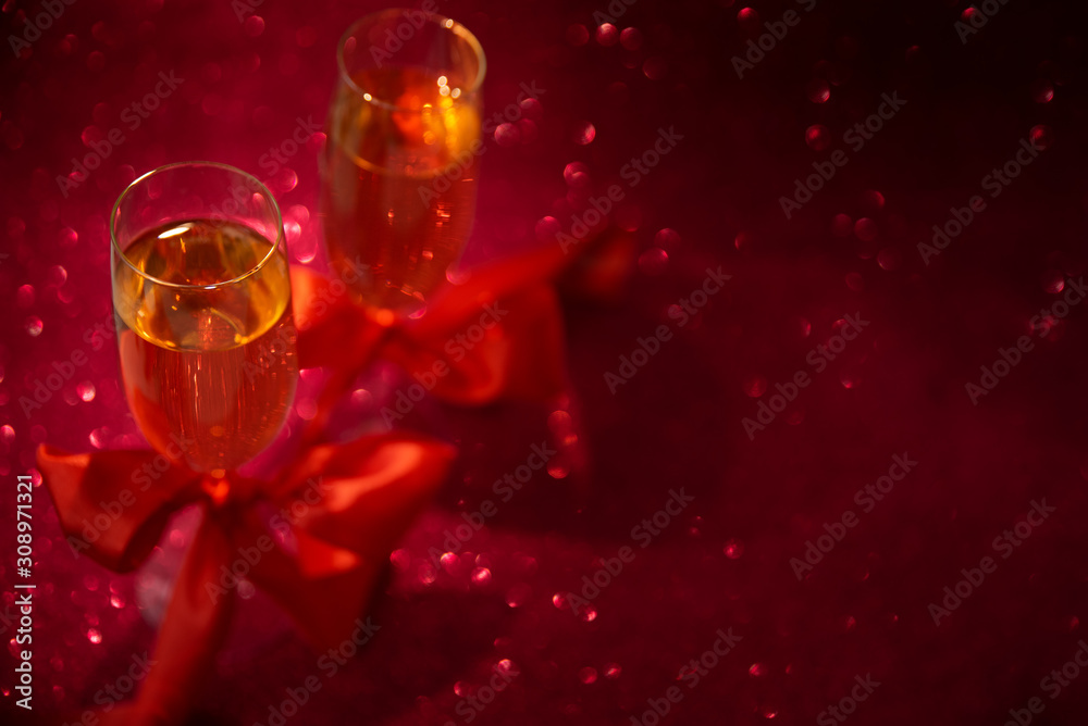 Two glasses of champagne decorated red ribbon on red glittering background. Valentines day or Wedding celebration concept. Copy space. Soft focus Two glasses of champagne decorated red ribbon on red glittering background. Valentines day or Wedding celebration concept. Copy space. Soft focus