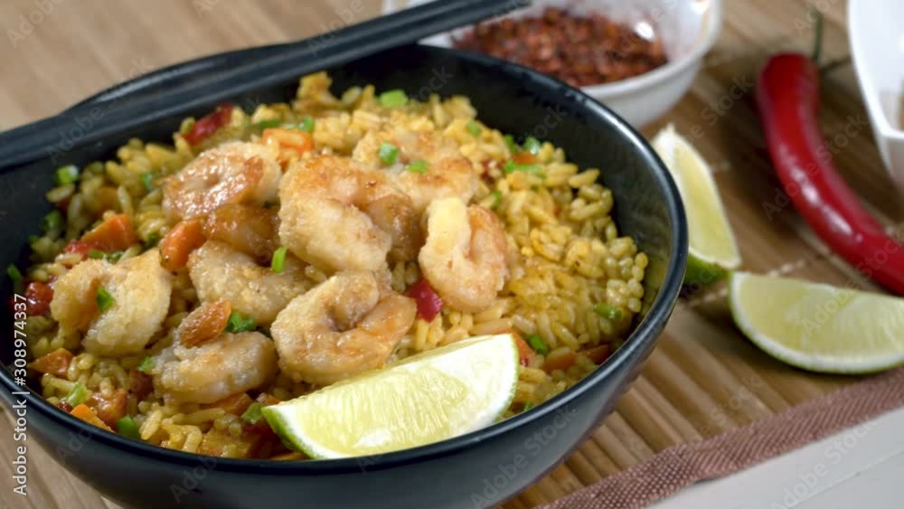 Traditional shrimps stir fried with eggs, vegetables and rice in a black bowl on a bamboo placemat. Healthy Asian meal with sesame and lime. Camera dolly and panning close-up follow focus shot. Traditional shrimps stir fried with eggs, vegetables and rice in a black bowl on a bamboo placemat. Healthy Asian meal with sesame and lime. Camera dolly and panning close-up follow focus shot.