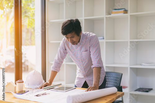  Man Architect or engineer hands working on blueprint plans with a pencil ,laptop a ruler, calculator, and engineering tools. Architect or engineer working on blueprint in office.