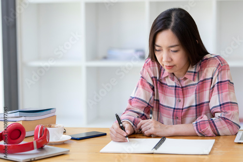 Asian woman writing something in her notebook. business women hand writing something on her paper note.