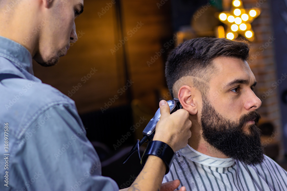 Step 2. Getting perfect shape step by step. Hair styling and cutting with  trimmer. Young apprentice giving haircut to bearded man at barber shop.  Advertising and barber shop concept. Stock Photo |