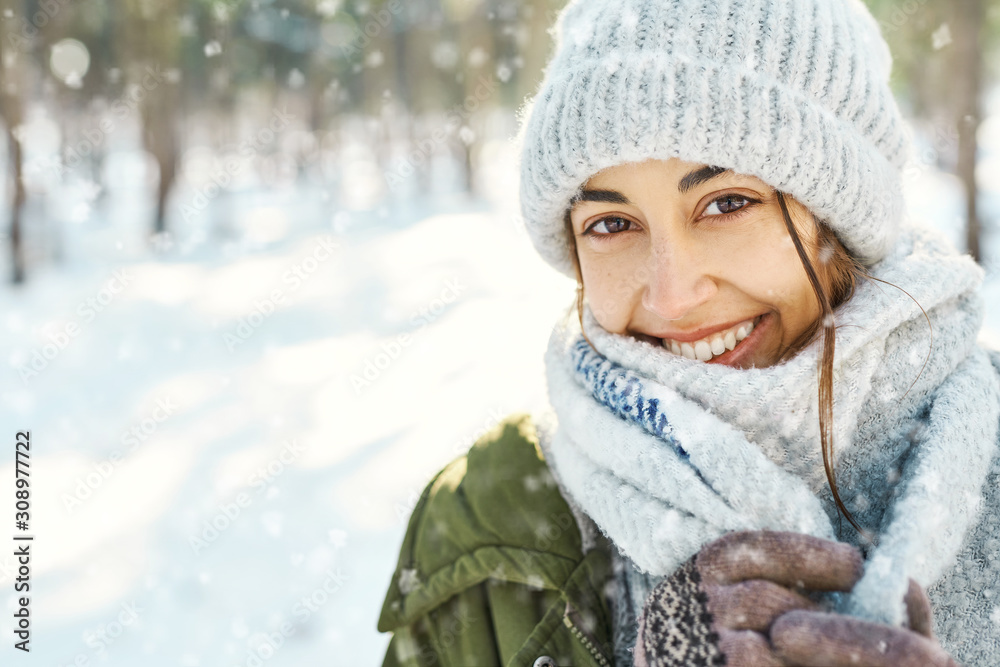 Closeup portrait of funny smiling woman in woolen hat and long warm scarf at snowy winter park in frozzy sunny day. Flying snowflakes. Happy winter time, having fun Closeup portrait of funny smiling woman in woolen hat and long warm scarf at snowy winter park in frozzy sunny day. Flying snowflakes. Happy winter time, having fun