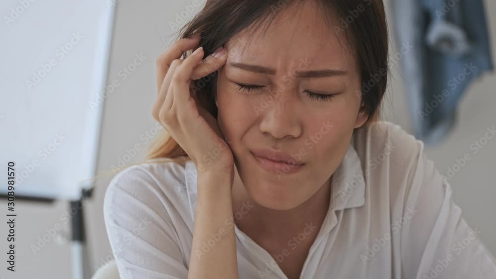 Tired asian business woman has a headache while sitting by the table in the office Tired asian business woman has a headache while sitting by the table in the office