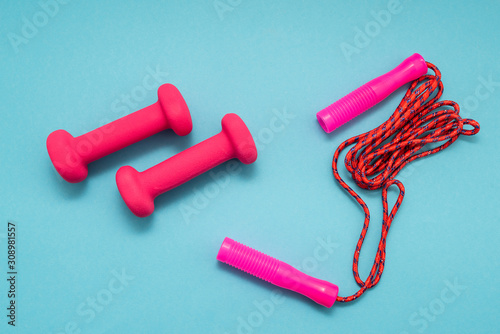 Pink dumbbells and jump rope on blue background.Sports, fitness and healthy lifestyle concept.