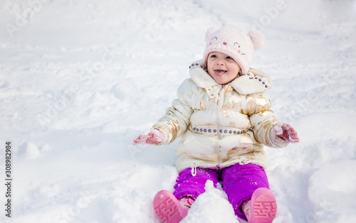 Little girl in white jacket having fun, playing outside, surrounded with snow.