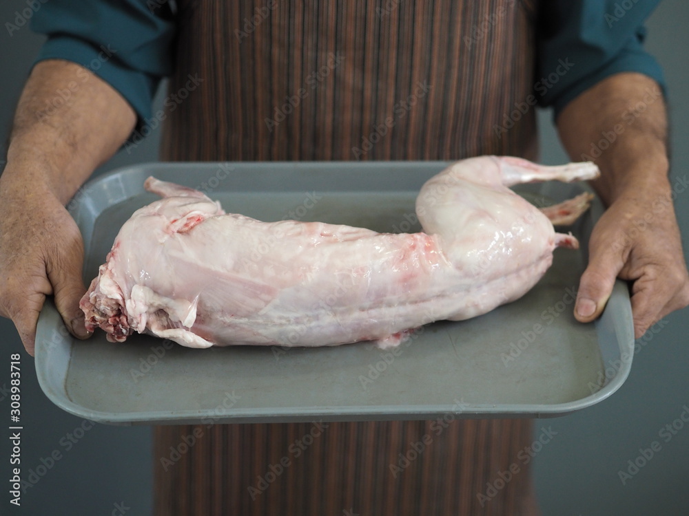 man’s hands carve raw rabbit meat into pieces