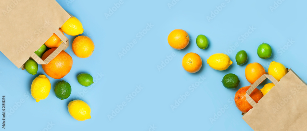 Creative background with tropical fruits. Orange, lemon, lime, grapefruit drop out of paper bag on blue background. Flat lay top view copy space. Food concept, vitamin C, disease prevention, flu