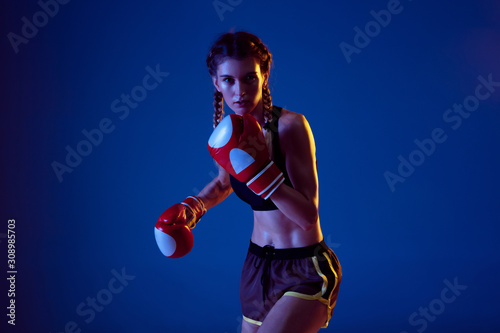 Practice. Fit caucasian woman in sportswear boxing on blue studio background in neon light. Novice female caucasian boxer working out and training. Sport, healthy lifestyle, movement concept.