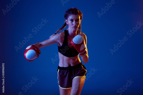 Beauty. Fit caucasian woman in sportswear boxing on blue studio background in neon light. Novice female caucasian boxer working out and training. Sport, healthy lifestyle, movement concept.