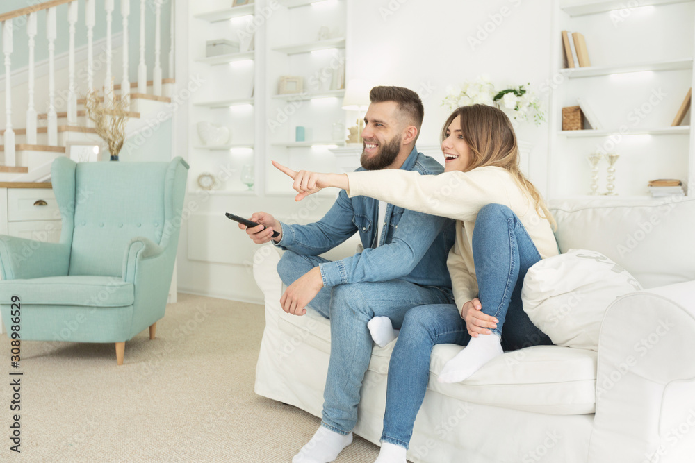 Young spouses watching tv, excited woman pointing at screen