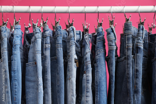 Rack with stylish jeans on pink background, closeup