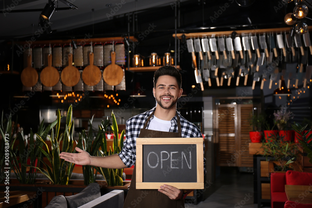 Naklejka premium Young business owner holding sign OPEN in his cafe