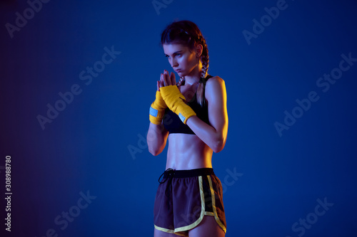 Fit caucasian woman in sportswear boxing on blue studio background in neon light. Novice female caucasian boxer preparing for working out and training. Sport, healthy lifestyle, movement concept.