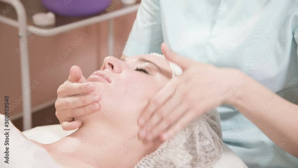 Girl beautician in a mask and gloves makes a salubrious facial massage to an attractive woman. New generation cosmetology massage Girl beautician in a mask and gloves makes a salubrious facial massage to an attractive woman. New generation cosmetology massage