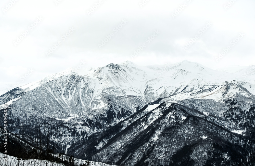 Winter snow-covered forest in the mountains. Snow-capped mountain peaks of the Caucasus mountain range near the resort of Arkhyz. Mountain peaks covered with snow in winter. Winter landscape.