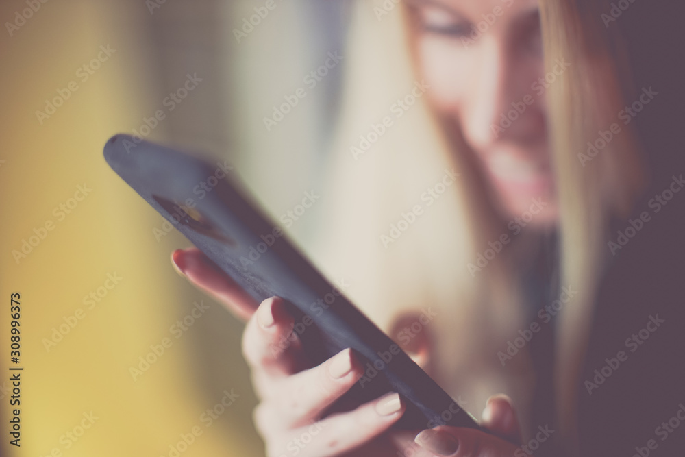 Smiling young blond woman use smartphone, soft selective focus on her fingers, blurred happy girl face.