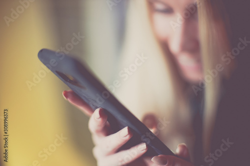 Smiling young blond woman use smartphone  soft selective focus on her fingers  blurred happy girl face.