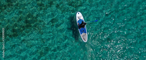 Aerial drone ultra wide photo of fit unidentified man practising in SUP board or Stand UP Paddle surf board in tropical exotic island turquoise sea