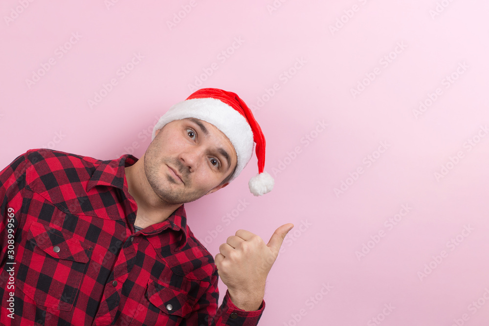 Emotions on the face, smile, joy. A man in a plaid rabbit and a Christmas red hat, on a pink background, copy space. Emotions on the face, smile, joy. A man in a plaid rabbit and a Christmas red hat, on a pink background, copy space.