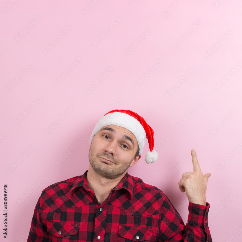 Emotions on the face, smile, joy. A man in a plaid rabbit and a Christmas red hat, on a pink background, copy space. Emotions on the face, smile, joy. A man in a plaid rabbit and a Christmas red hat, on a pink background, copy space.
