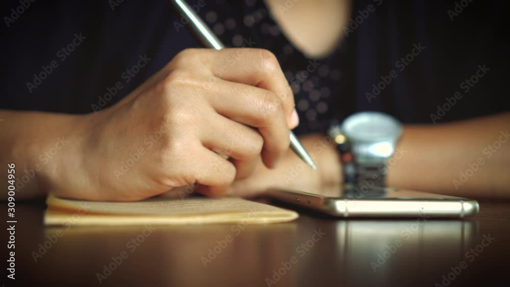 4k video woman hand writing down in white notebook while using smartphone to plan work on table with bokeh light in cafe background. 4k video woman hand writing down in white notebook while using smartphone to plan work on table with bokeh light in cafe background.