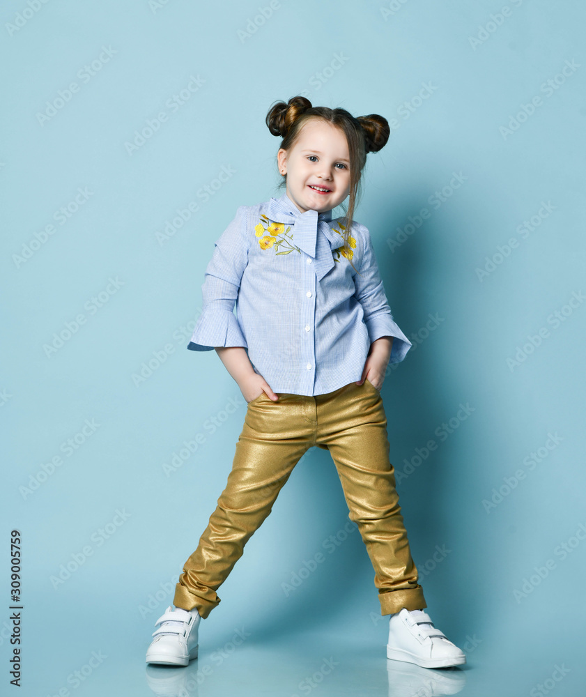 Active cheerful baby kid girl in blue shirt and gold leather pants is cool  posing with her hands in her pockets, smiling Stock Photo