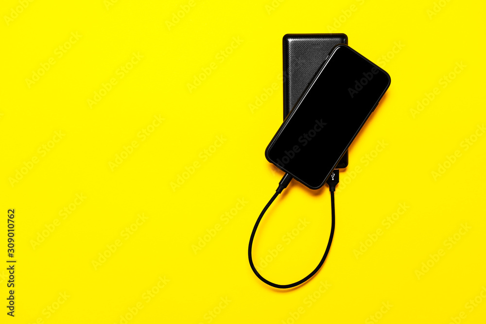 Black Power bank charges smartphone isolated on yellow background Black Power bank charges smartphone isolated on yellow background