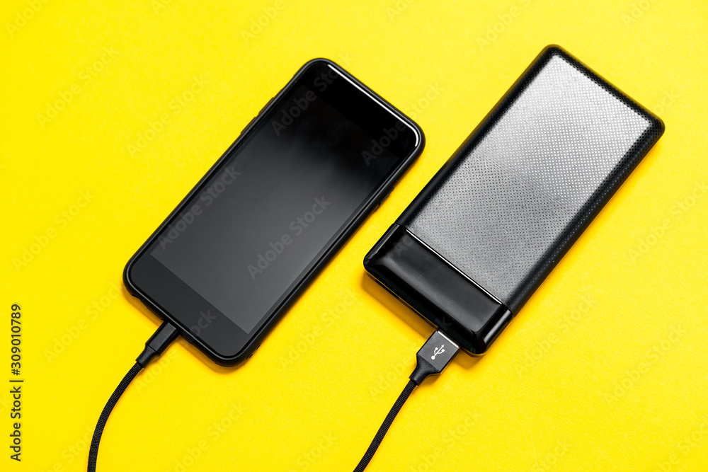 Black Power bank charges smartphone isolated on yellow background Black Power bank charges smartphone isolated on yellow background