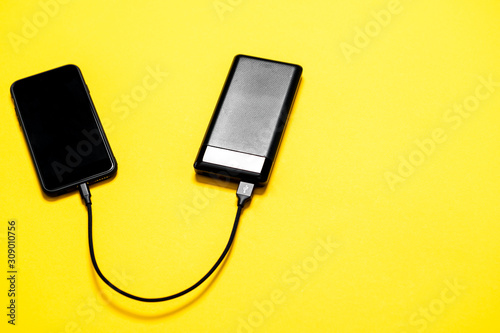 Black Power bank charges smartphone isolated on yellow background