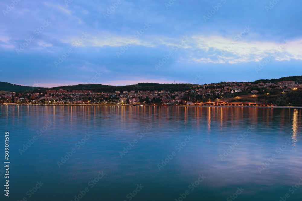 Fototapeta premium Picturesque landscape of Koper at night. Illumination of the city reflected in water of the Adriatic Sea. Famous touristic place and travel destination in Europe
