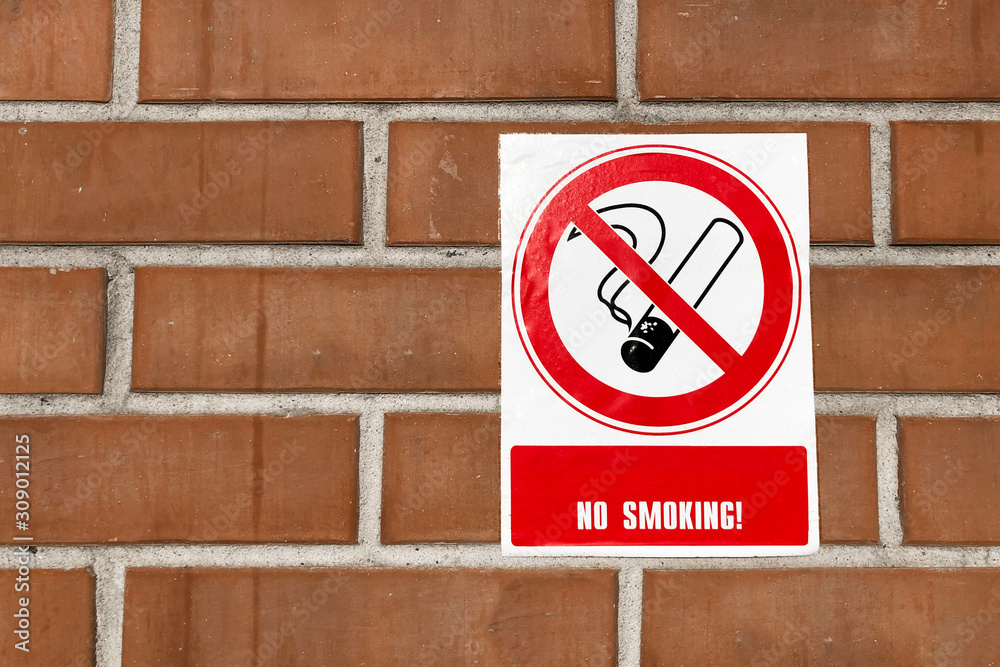 no smoking inscription or no smoking sign on the antique orange brick wall. placard with smoking cigarette crossed out, dirty brick wall in the background. no smoking inscription or no smoking sign on the antique orange brick wall. placard with smoking cigarette crossed out, dirty brick wall in the background.