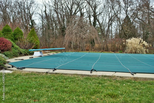 backyard swimming pool with diving board and pool slide tarped up and closed down for winter