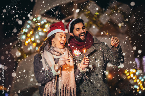Young loving couple burning sparklers by holiday illumination on New Years eve.