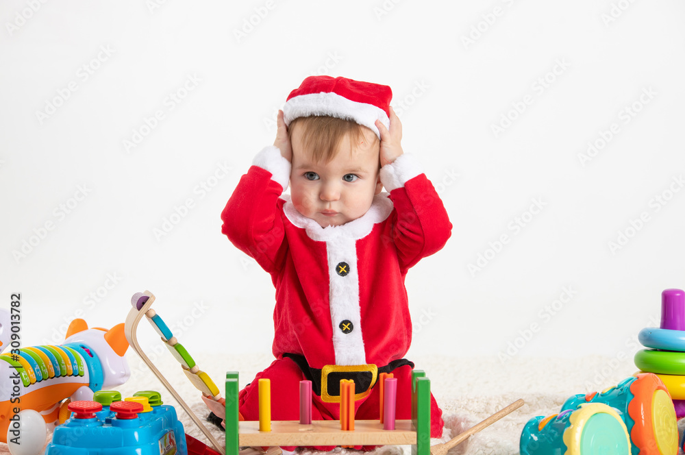 Baby dressed as Santa Claus sitting on a blanket playing with wooden and plastic toys Baby dressed as Santa Claus sitting on a blanket playing with wooden and plastic toys