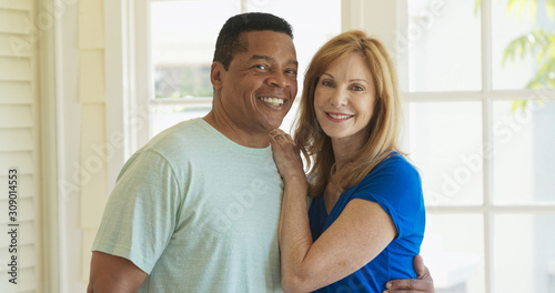 Portrait of mixed race senior couple looking at camera and holding each other