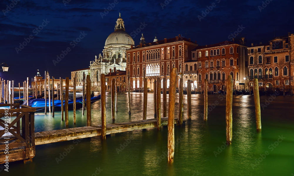 Nighttime panorama of cathedral of Santa Maria della Salute in Venice old town, Italy. Antique medieval building with dome at banks of Grand Canal. View from canal with water waves. Famous landmark.